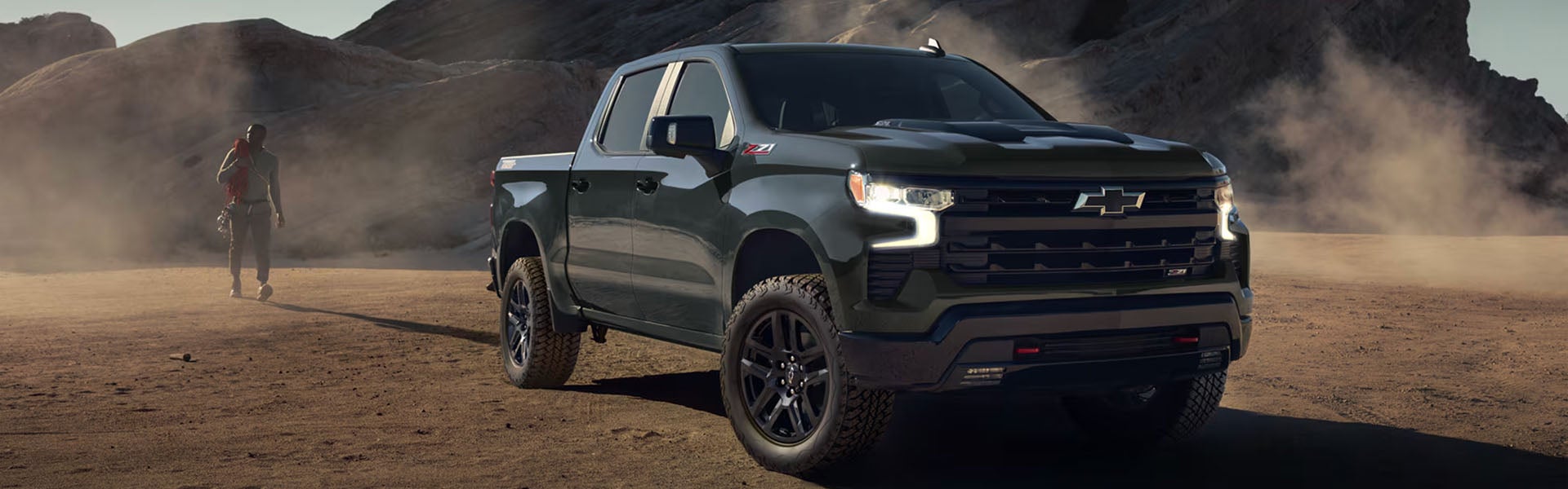 Used Dark green Chevrolet Silverado 1500 truck parked in a dusty desert landscape.
