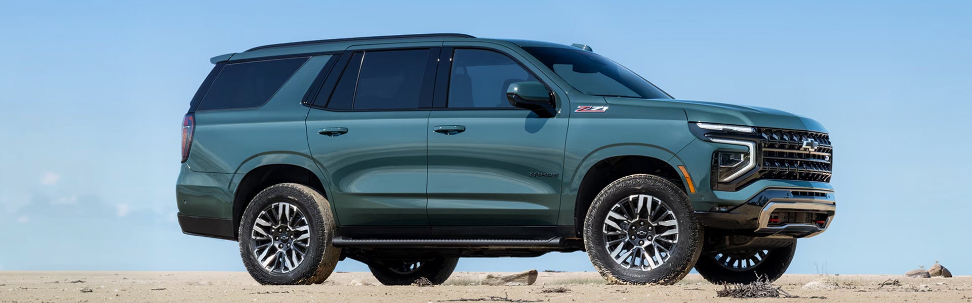 Green Chevrolet Tahoe SUV parked on a sandy terrain under a clear blue sky.