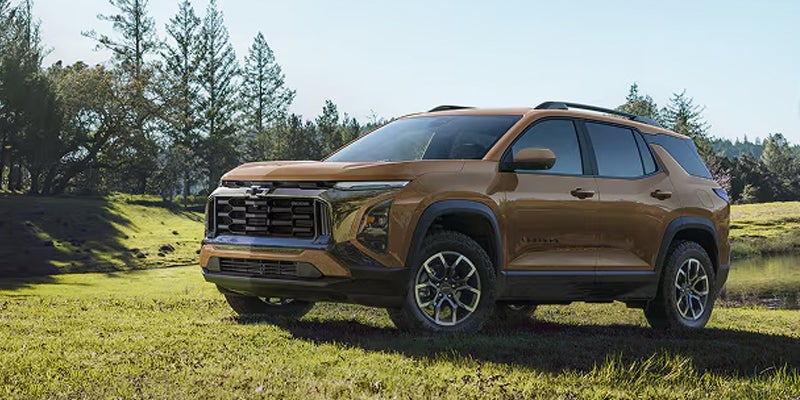 A bronze-gold Chevrolet Equinox ACTIV SUV parked on a grassy field near a treeline.