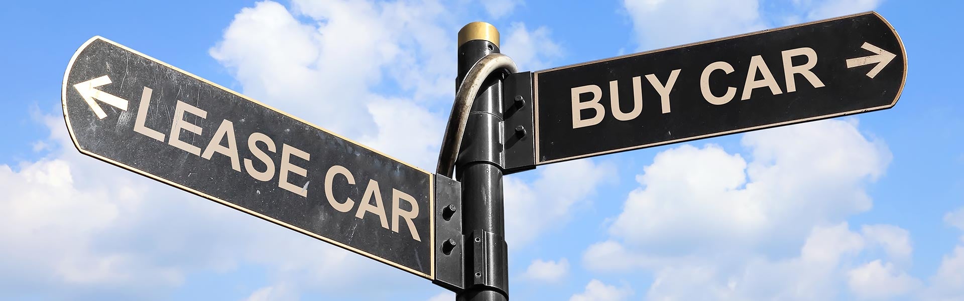 Directional street sign with arrows pointing to "LEASE CAR" and "BUY CAR" against a blue sky.